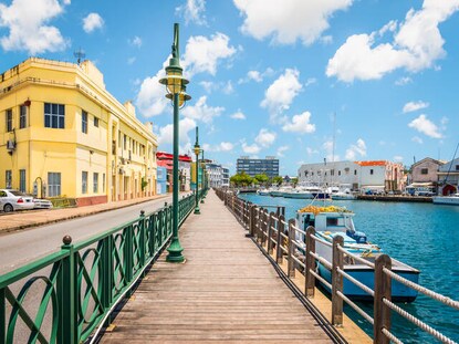 Shot of Bridgetown Boardwalk with buildings on one side and water and boats on the other in Barbados. 