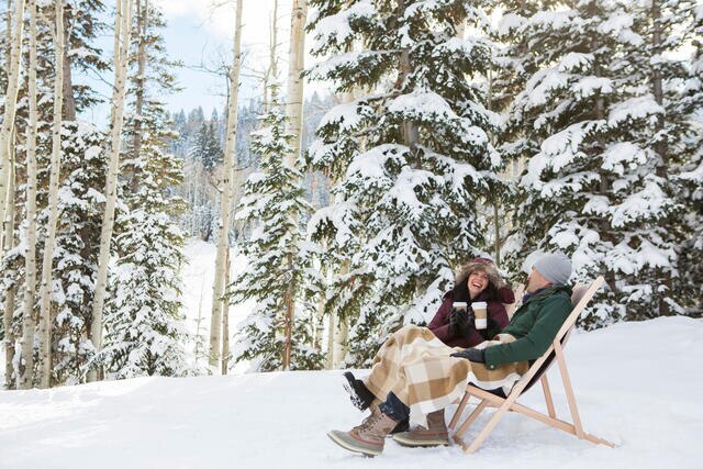 Couple happily enjoying an aprés ski beverage outside in the snow. 