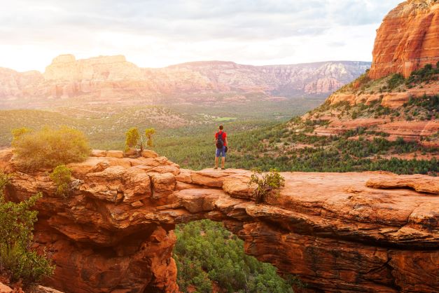 Man standing atop a giant Sedona red rock  and enjoying the view after a hike, Arizona. 