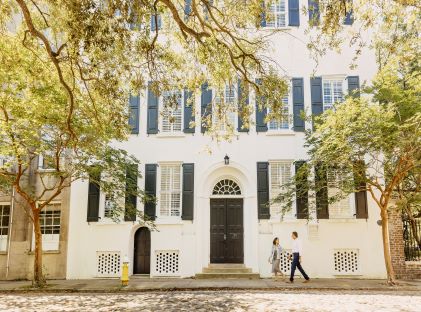 A couple stands in front of a white building in Charleston, South Carolina