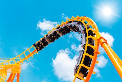 A bright yellow rollercoaster at theme park has an coaster cart on the track going through a twist 