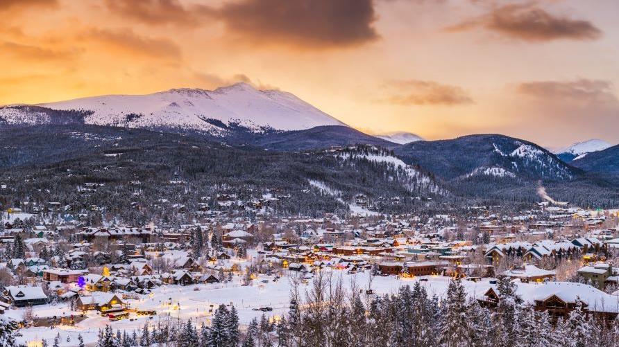 Stunning aerial image, snow-covered mountain town, snow-capped mountains in distance, cotton candy skies overhead, Breckenridge, Colorado. 