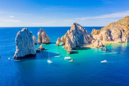 Stunning aerial image, the Arch of Cabo San Lucas, blue skies, boats peppering clear blue water, Mexico. 
