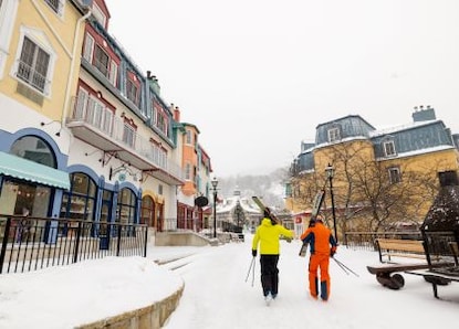 Winter scene, two skiiers carrying skies through snow-covered, mainstreet, village center, Mont-Tremblant, Quebec, Canada. 