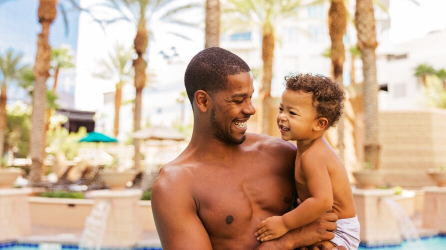 African American man holding a toddler in his arms by the swimming pool