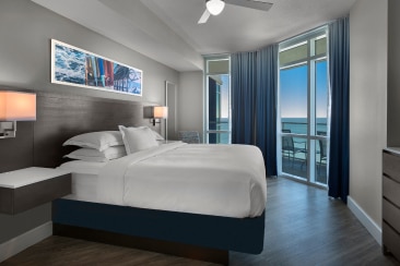 Queen-size bed in a bedroom with a view to the sea through balcony doors