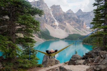Young man sitting in a hammock looking out over a mountain lake
