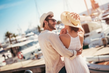 A man and woman couple wearing hats, and embracing on the docks, surrounded by boats.